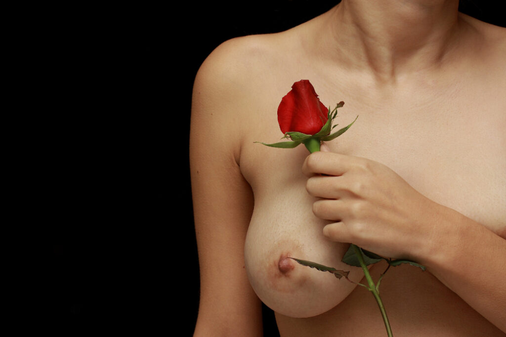 Woman holding a rose next to her breast.